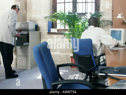 Two men in a room, one using computer, rear view Stock Photo