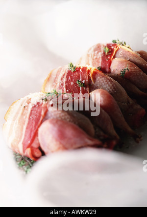 Three whole raw quails in a line, wrapped with bacon and sprinkled with herbs Stock Photo