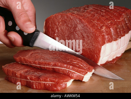 Fingers holding knife, slicing raw beef fillets, close-up Stock Photo