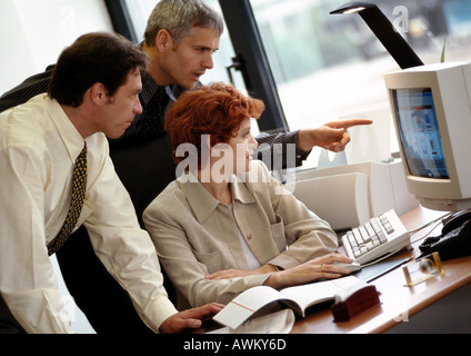 Two businessmen and a businesswoman looking at computer screen Stock Photo