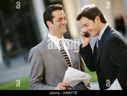 Two businessmen side by side outside, one using cell phone Stock Photo