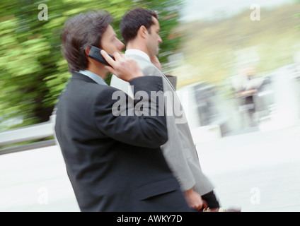 Two businessmen walking outside, using cell phones, side view Stock Photo