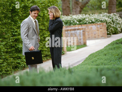 Businessman and businesswoman standing in park, businesswoman using cell phone Stock Photo