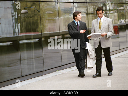 Two businessmen walking along sidewalk in front of building Stock Photo
