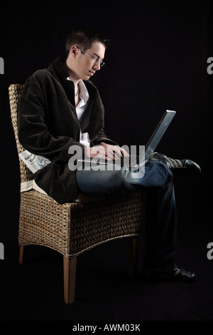 Young man sitting on a chair with a laptop on his lap Stock Photo