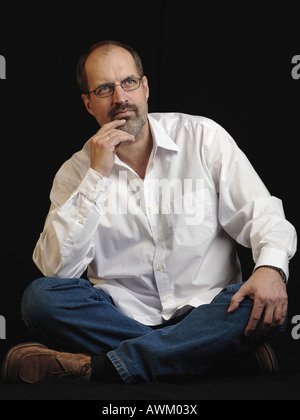 Thoughtful middle-aged man sitting cross-legged Stock Photo