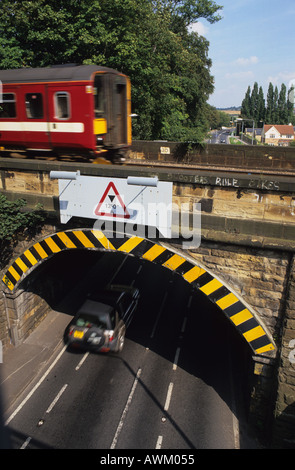 vehicle passing under low railway bridge with train passing over the top leeds uk Stock Photo