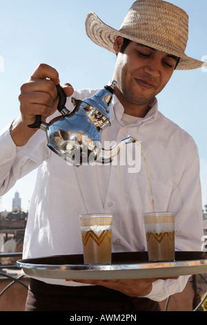 Waiter wearing straw hat pouring mint tea in the historic Medina quarter, Marrakesh, Morocco, Africa Stock Photo