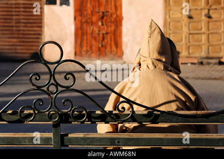 Moroccan man wearing a Djellaba taking a rest on a wrought iron bench, Medina, Marrakech, Morocco, Africa Stock Photo