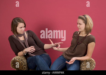 Two girls, pre-teens, early teens sitting on a tiger-print couch talking Stock Photo