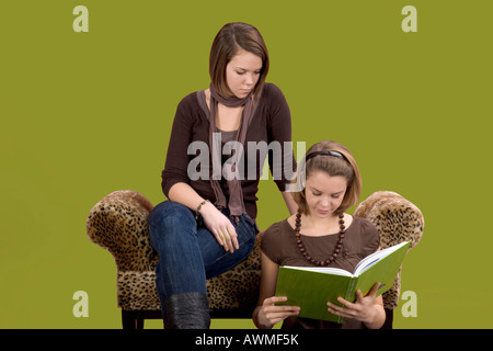 Two girls, pre-teens, early teens sitting on a tiger-print couch reading a book Stock Photo