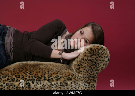 Portrait of a girl, pre-teen, early teens laying on a tiger-print sofa Stock Photo