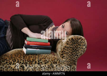 Portrait of a girl, pre-teen, early teens laying on a tiger-print sofa with a stack of schoolbooks Stock Photo