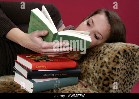 Portrait of a girl, pre-teen, early teens laying on a tiger-print sofa with a stack of schoolbooks Stock Photo