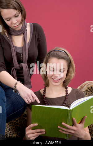 Two girls, pre-teens, early teens sitting on a tiger-print sofa reading a book Stock Photo