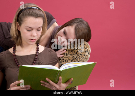 Two girls, pre-teens, early teens sitting on a tiger-print sofa reading a book Stock Photo