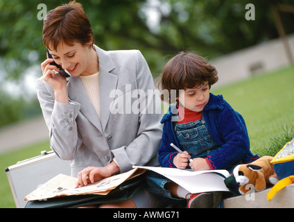 Businesswoman and child sitting outside together, woman using cell phone Stock Photo