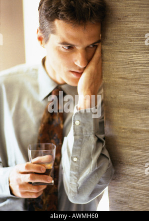 Man with hand against face leaning against wall and holding glass, close-up Stock Photo