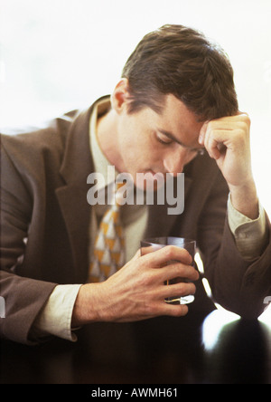 Man sitting with head against hand, holding glass, head and shoulders, close-up Stock Photo