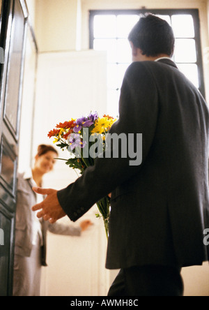 Man holding bouquet, woman smiling in background, rear view Stock Photo