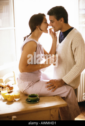 Woman sitting on table, feeding croissant to man Stock Photo