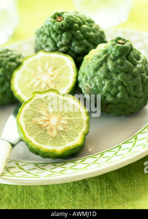 Kaffir limes, one cut in half, on plate, close-up Stock Photo