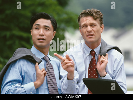 Two business associates standing outdoors having discussion, holding jackets over shoulder Stock Photo