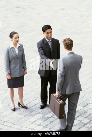 Businesswoman standing beside two businessmen shaking hands, elevated view Stock Photo