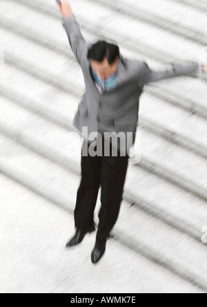 Businessman arms outstretched, jumping near steps, blurred Stock Photo