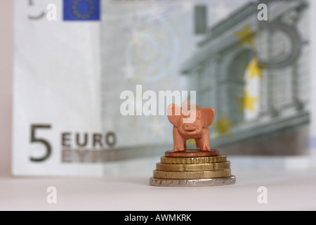 Rubber pig on a pile of coins, a Five-Euro note in the background Stock Photo