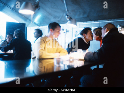Young people sitting at table, couple kissing Stock Photo