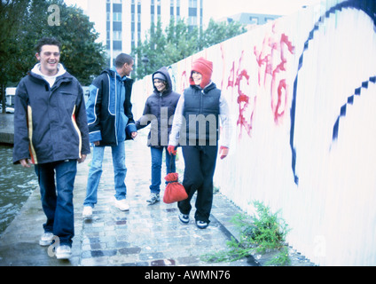 Four young people walking on sidewalk next to graffiti-covered wall Stock Photo
