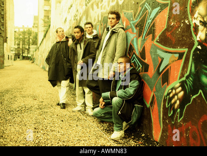 Five young men leaning against wall covered in graffiti, full length Stock Photo