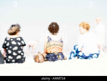 People sitting on sand at the beach, rear view, blurred Stock Photo