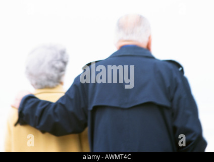 Elderly man and woman, man's arm around woman's shoulder, rear view, blurred and backlit Stock Photo