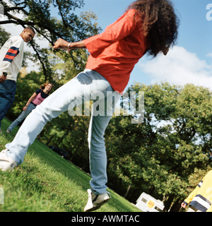Young people together outside, young woman jumping in foreground, rear view Stock Photo