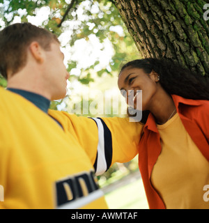 Young woman leaning against tree looking up at young man Stock Photo