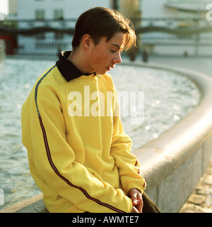 Teenage boy sitting on edge of fountain, looking down. Stock Photo