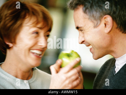 Man and woman smiling at each other, holding apple between them, close up, blurred Stock Photo