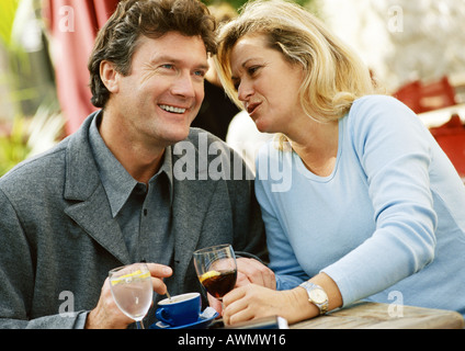 Man and woman sitting at table, woman whispering to man,  close-up Stock Photo