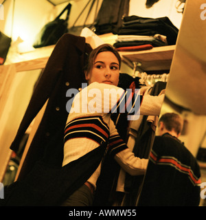 Young woman in clothing store looking over shoulder, young man reflected in mirror Stock Photo
