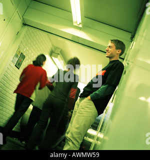 Young man standing in subway corridor, side view, people walking, rear view in background Stock Photo