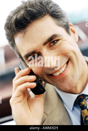 Businessman using cellular phone, smiling at camera, close-up, portrait. Stock Photo