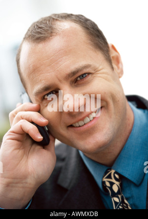 Businessman using cellular phone, smiling at camera, portrait, close-up. Stock Photo