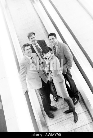 Group of business people on moving walkway smiling at camera, business woman in front on cell phone, b&w. Stock Photo