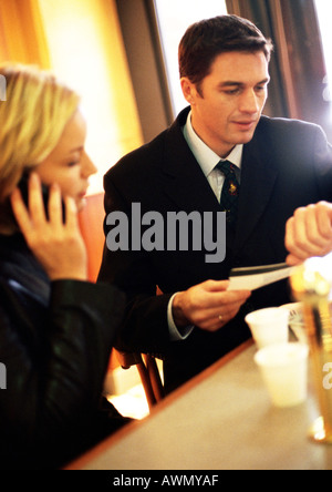 Businesswoman on cell phone next to businessman holding ticket and looking down at watch Stock Photo