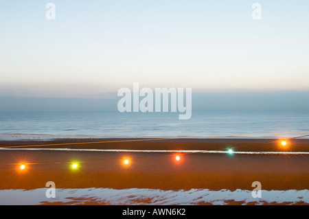 String of electric lights against beach and sea at dusk Stock Photo