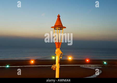 String of electric lights attached to lamp post against beach and sea at dusk Stock Photo