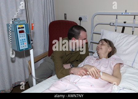 A patient shares a joke with her partner (husband) and smiles whilst she is on a chemotherapy drip Stock Photo