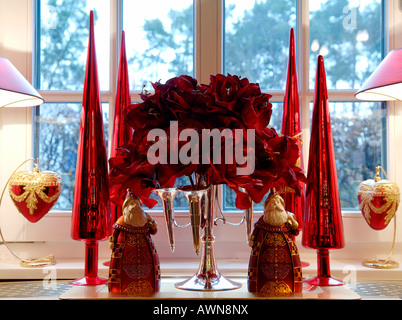Christmas decorations in front of a window, two Santas stylized Christmas trees, red artificial flowers in a four-armed candela Stock Photo